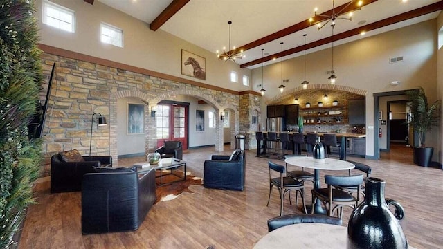 living room featuring arched walkways, a notable chandelier, wood finished floors, a towering ceiling, and beamed ceiling