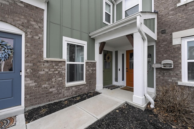 view of exterior entry featuring board and batten siding and brick siding