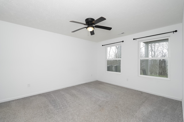 carpeted empty room featuring a textured ceiling, visible vents, a ceiling fan, and baseboards