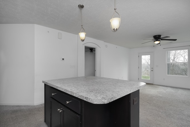 kitchen featuring dark cabinets, light countertops, light carpet, and hanging light fixtures