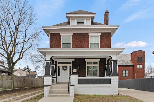 traditional style home featuring covered porch, a chimney, fence, and brick siding