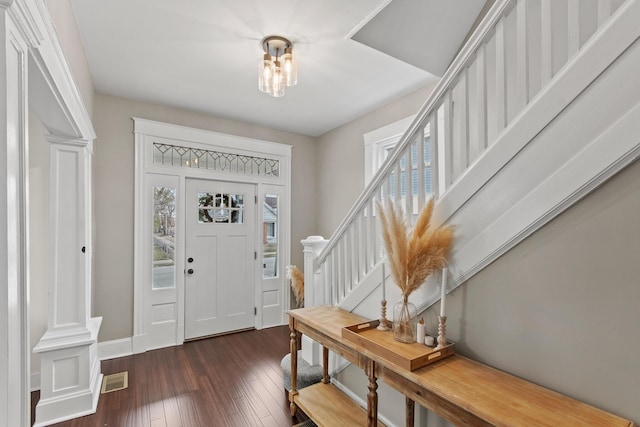 entrance foyer with dark wood-style flooring, visible vents, baseboards, stairs, and ornate columns