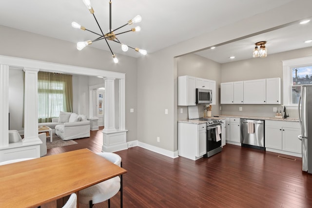 kitchen with dark wood-style flooring, stainless steel appliances, white cabinetry, a sink, and ornate columns