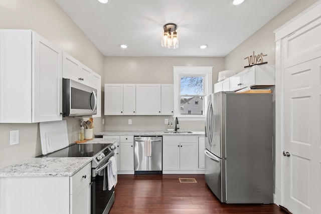 kitchen with a sink, white cabinetry, appliances with stainless steel finishes, light stone countertops, and dark wood finished floors