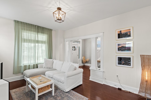 living area featuring a wealth of natural light, dark wood finished floors, decorative columns, and an inviting chandelier