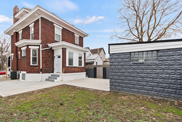 view of property exterior with brick siding, a chimney, central AC, a patio area, and fence