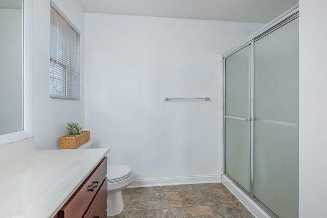 bathroom with baseboards, toilet, a shower with shower door, stone finish flooring, and vanity