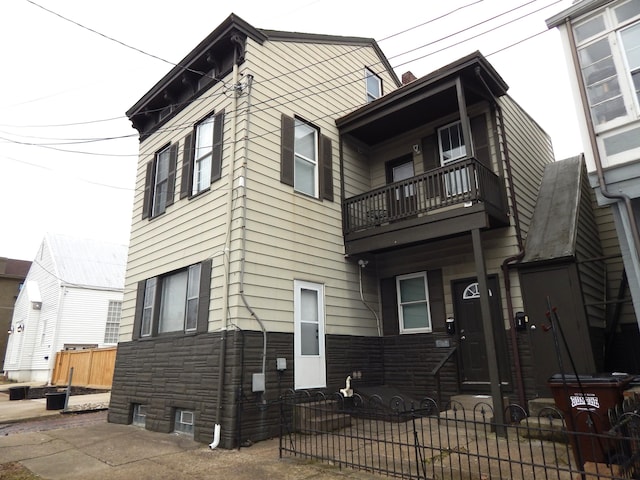 view of front facade featuring a balcony, stone siding, and a fenced front yard