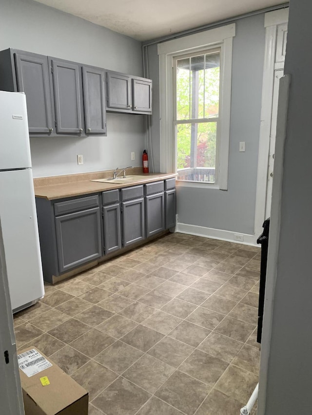 kitchen featuring baseboards, gray cabinets, light countertops, and freestanding refrigerator