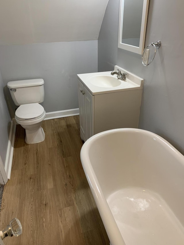 full bath featuring lofted ceiling, toilet, wood finished floors, a freestanding bath, and vanity