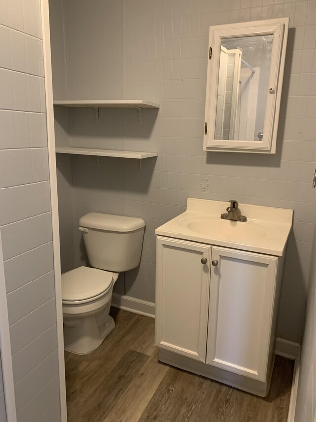 bathroom featuring toilet, tile walls, wood finished floors, and vanity