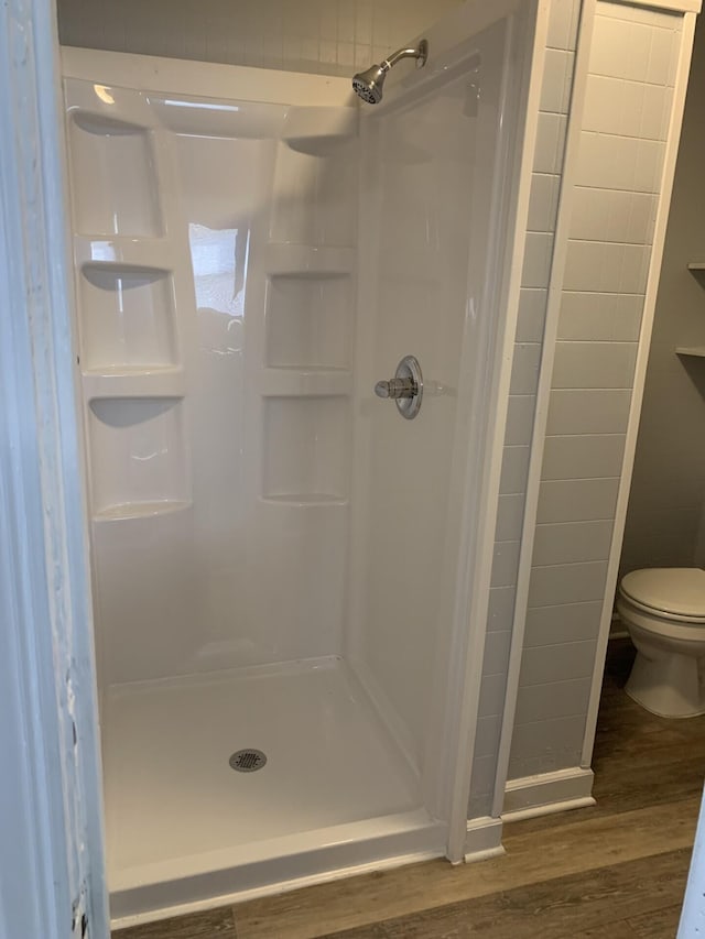 bathroom with toilet, a shower stall, and wood finished floors