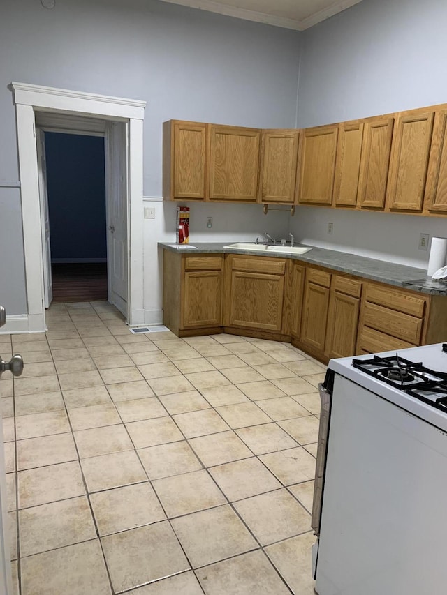 kitchen with light tile patterned floors, white range with gas cooktop, brown cabinetry, ornamental molding, and a sink