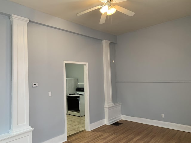 spare room featuring wood finished floors, visible vents, baseboards, a ceiling fan, and decorative columns