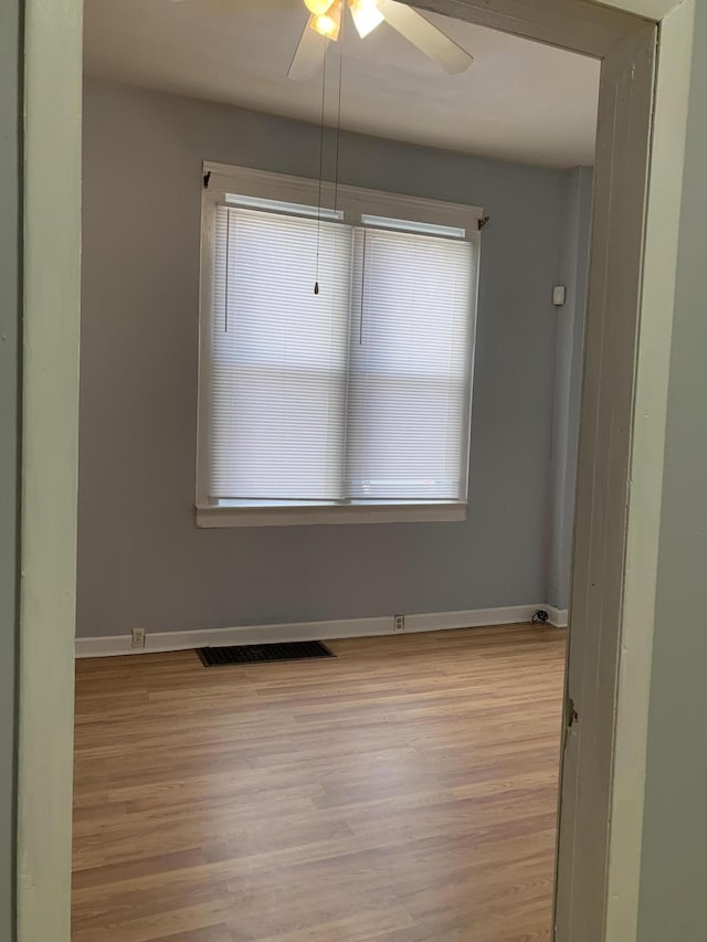 empty room featuring a wealth of natural light, light wood-style flooring, visible vents, and baseboards