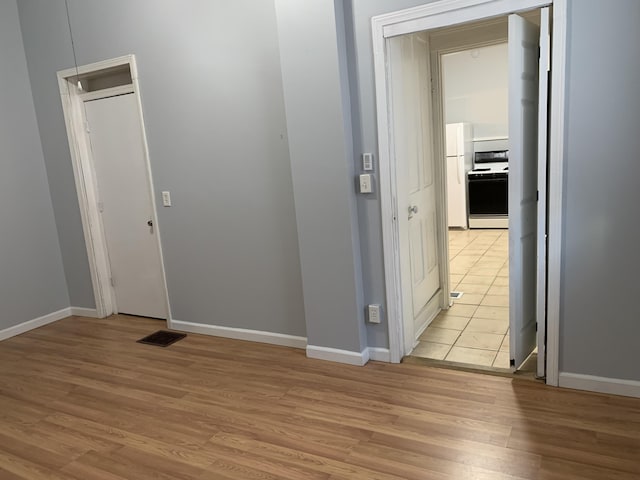 hallway with visible vents, light wood-style flooring, and baseboards