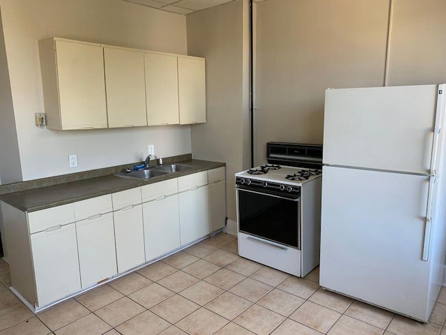 kitchen featuring light tile patterned floors, white appliances, dark countertops, and a sink