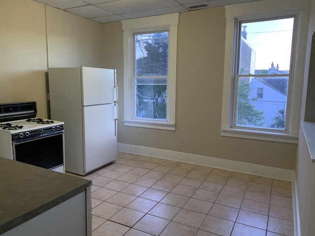 kitchen featuring white appliances, baseboards, a drop ceiling, dark countertops, and light tile patterned flooring