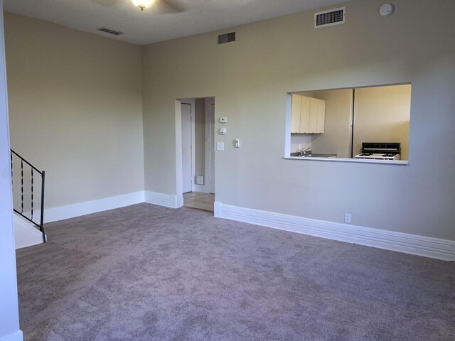 empty room with carpet floors, visible vents, baseboards, and stairs