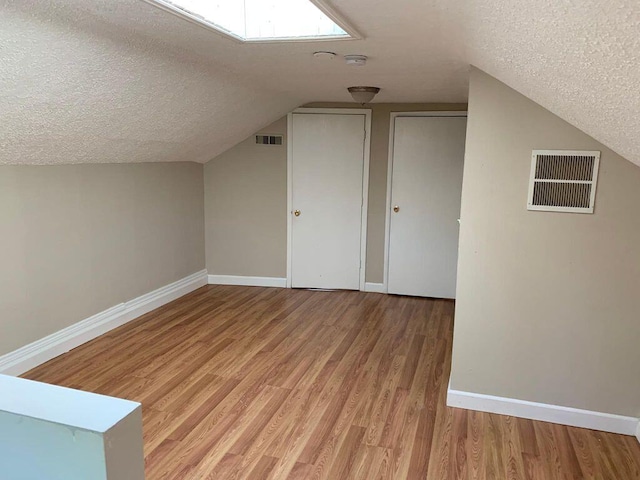 additional living space with light wood-type flooring, baseboards, visible vents, and a textured ceiling