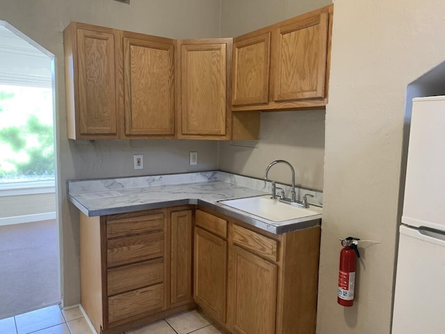 kitchen with baseboards, light tile patterned flooring, a sink, and freestanding refrigerator