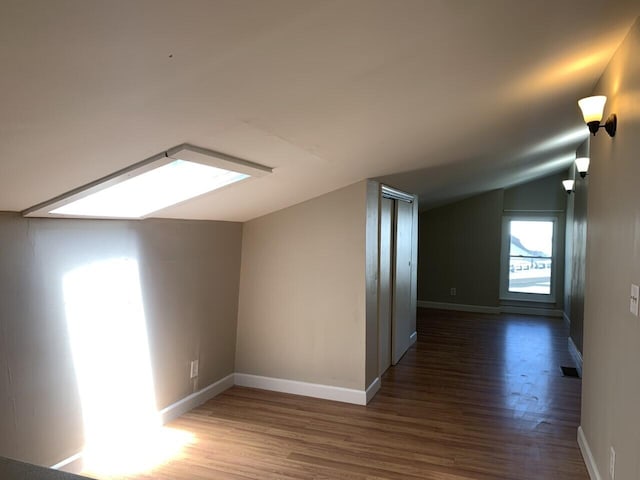 additional living space with lofted ceiling with skylight, wood finished floors, and baseboards