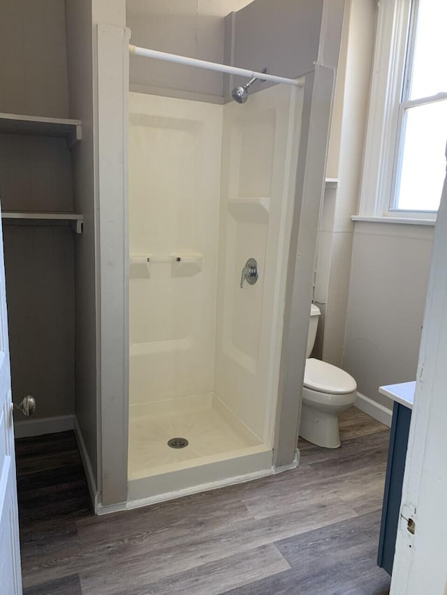 bathroom featuring toilet, wood finished floors, vanity, baseboards, and a stall shower