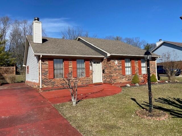 ranch-style home with roof with shingles, brick siding, a chimney, and a front yard