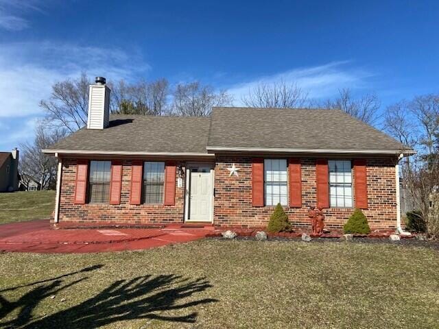 view of front of home featuring brick siding, a chimney, a front lawn, and roof with shingles