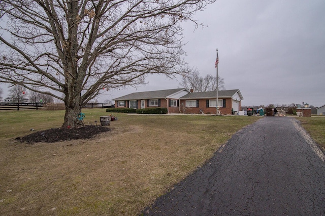 ranch-style house with aphalt driveway, fence, a front lawn, and brick siding