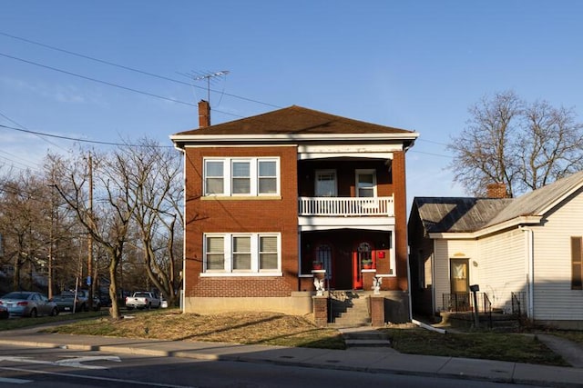 view of front of home with brick siding, a chimney, and a balcony