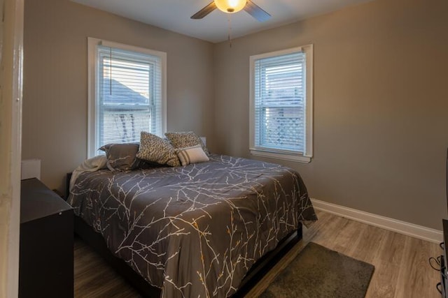 bedroom with multiple windows, ceiling fan, baseboards, and wood finished floors