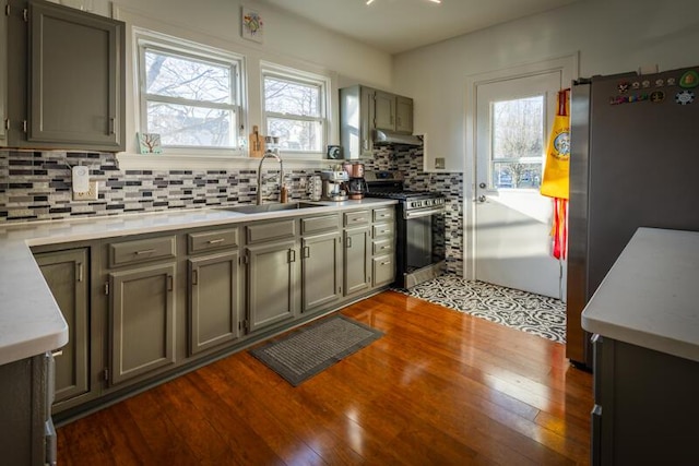 kitchen featuring a sink, under cabinet range hood, stainless steel appliances, decorative backsplash, and dark wood-style flooring