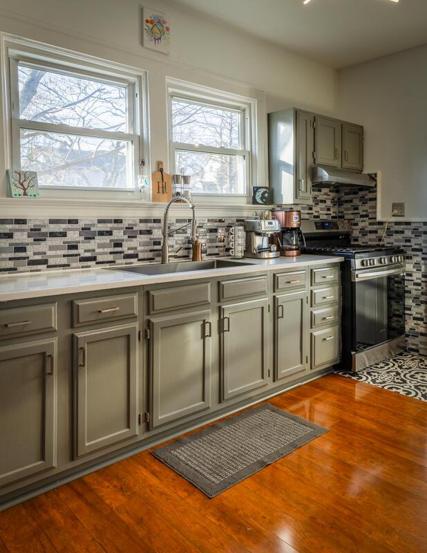 kitchen with gray cabinets, a sink, under cabinet range hood, wood finished floors, and gas range