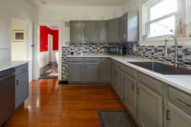 kitchen with dark wood finished floors, gray cabinetry, stainless steel appliances, light countertops, and a sink