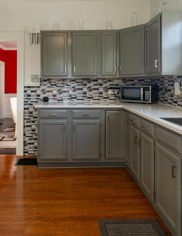 kitchen with stainless steel microwave, light countertops, gray cabinets, and dark wood-style flooring