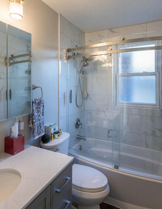 full bathroom with combined bath / shower with glass door, toilet, and vanity