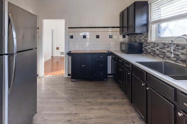 kitchen featuring a sink, light wood finished floors, black microwave, and freestanding refrigerator