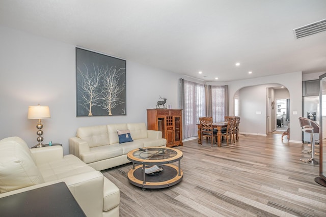 living area featuring visible vents, arched walkways, baseboards, light wood-style flooring, and recessed lighting