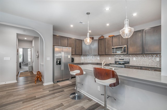 kitchen featuring dark brown cabinetry, visible vents, decorative backsplash, stainless steel appliances, and a sink