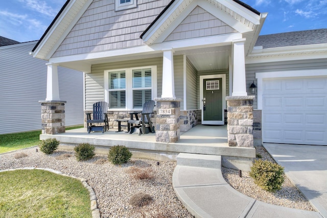 view of exterior entry with a garage, stone siding, and a porch