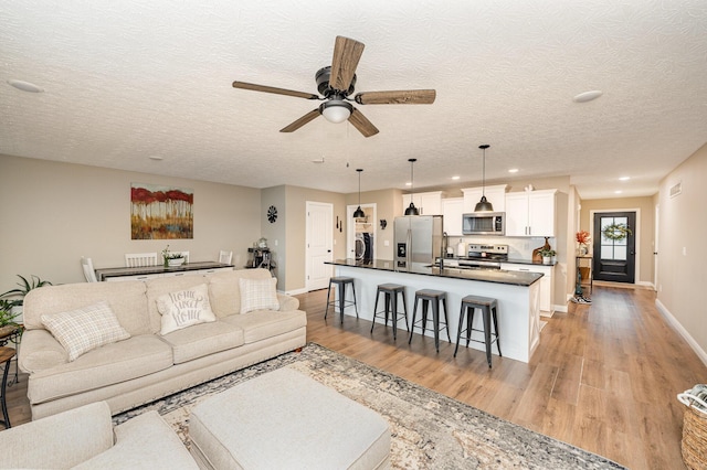 living room with light wood-style floors, washer / clothes dryer, ceiling fan, and baseboards