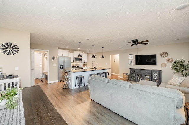 living area with light wood-style floors, a ceiling fan, baseboards, and a textured ceiling