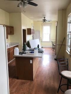 kitchen with brown cabinetry, ceiling fan, wood finished floors, freestanding refrigerator, and light countertops