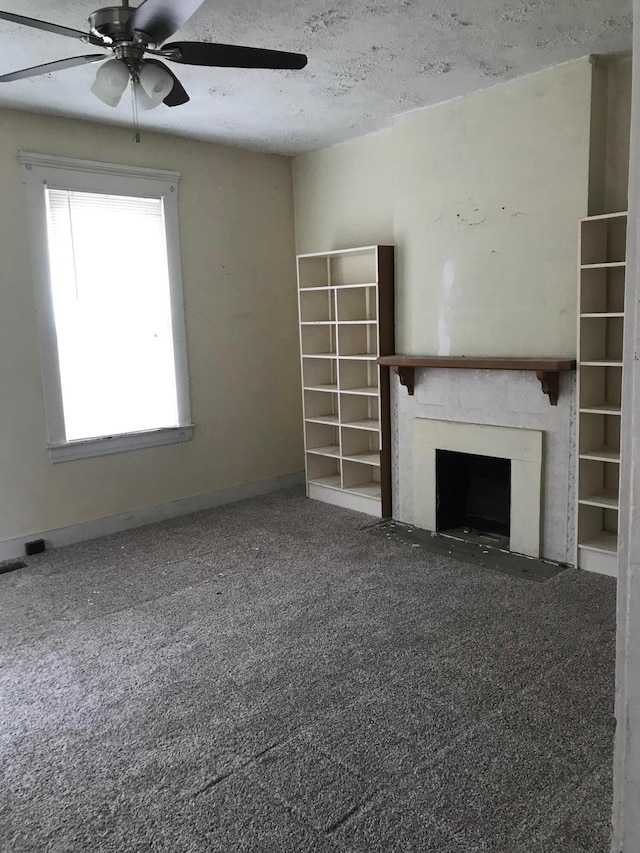 unfurnished living room with a textured ceiling, a fireplace, a ceiling fan, baseboards, and carpet