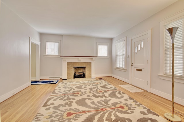 unfurnished living room with a baseboard radiator, a fireplace, baseboards, and wood finished floors