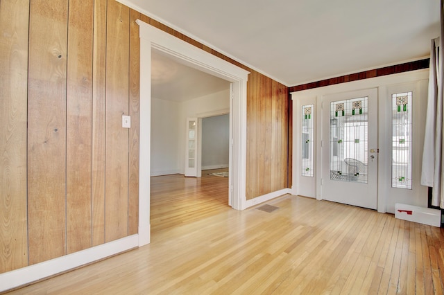 entrance foyer with baseboards, visible vents, wooden walls, and hardwood / wood-style floors