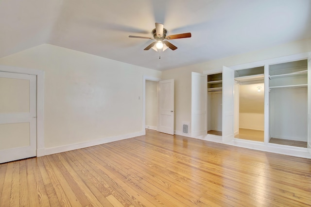 unfurnished bedroom with baseboards, visible vents, vaulted ceiling, light wood-type flooring, and multiple closets