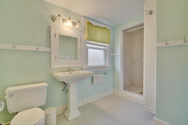 bathroom featuring toilet, a sink, tiled shower, baseboards, and tile patterned floors