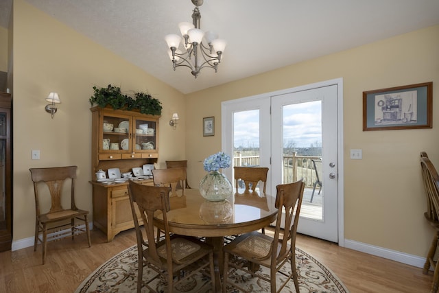 dining space featuring a chandelier, light wood-type flooring, lofted ceiling, and baseboards